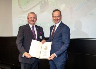 Dr. Volker Wissing und Prof. Reimund Neugebauer halten gemeinsam den Förderbescheid in den Händen und schauen in die Kamera